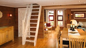 L’intérieur d’un chalet en bois, avec un escalier en bois, une table à manger entourée de chaises, un canapé et une cheminée.