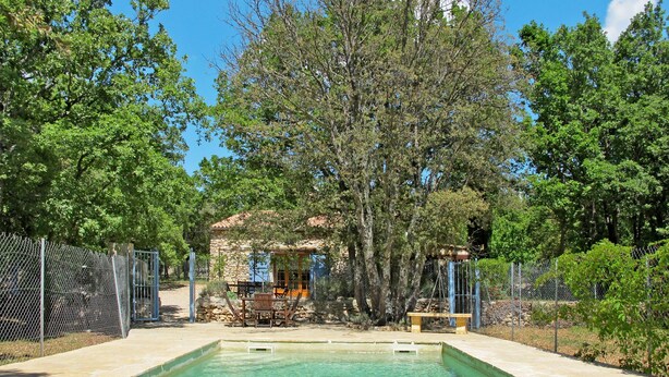 Una piscina con una estructura de piedra y zona de estar rodeada de árboles.