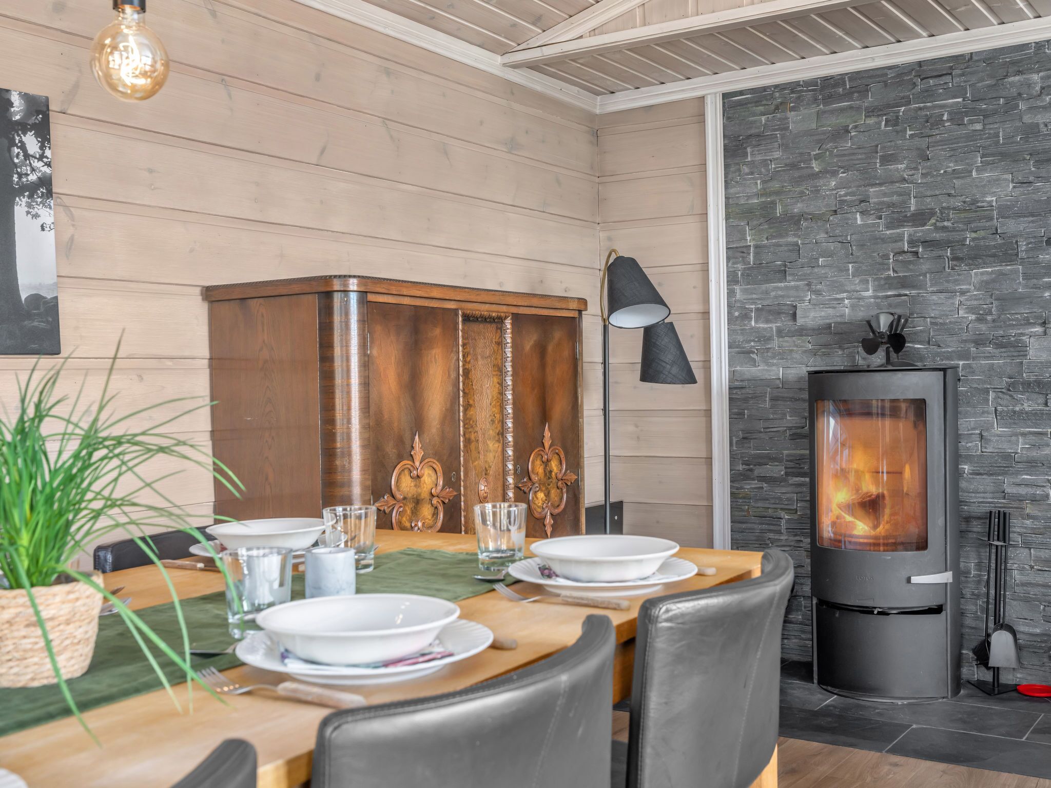 A dining area with a wooden table set for four, a decorative cabinet, a modern fireplace, and a potted plant.