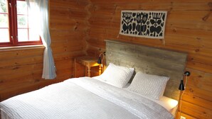 Una camera di una baita in legno con un letto, una finestra con tende, un decoro a parete e lampade da comodino.