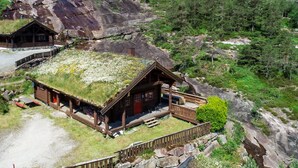 Una baita con tetto in erba, terrazza in legno e vista sulle montagne e sulla foresta circostanti.