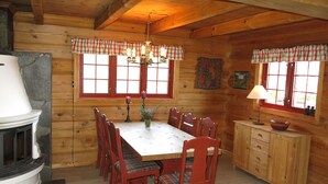Interno di una baita in legno con tavolo da pranzo, sedie, camino e angolo cottura.