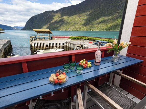 A balcony with a table set with food, a bottle, and flowers, overlooking a lake and mountains.