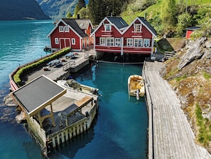 A wooden dock with a boat, a red house with a balcony, and a small shed.