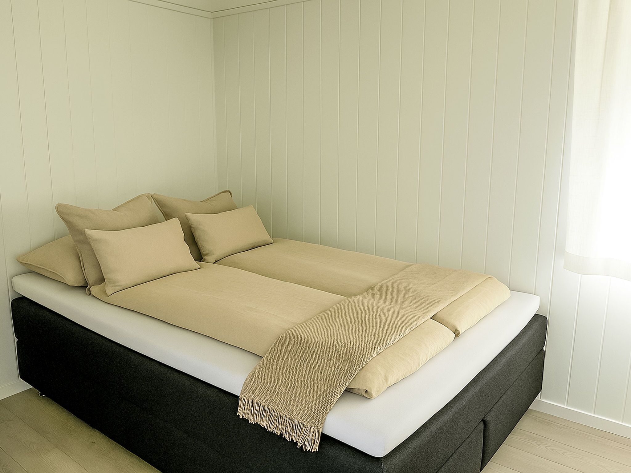 A bed with a black frame, beige bedding, and a beige throw blanket.