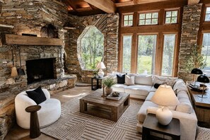 A stone fireplace, a stone wall, a large window, and a white sofa.