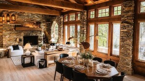 Un intérieur rustique avec des murs en pierre, des poutres en bois, une cheminée et un coin repas aménagé pour le dîner.