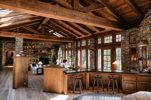 Ein rustikaler Innenraum mit freiliegenden Holzbalken, Steinwänden, einem Kamin aus Stein und einer Bar mit Hockern.