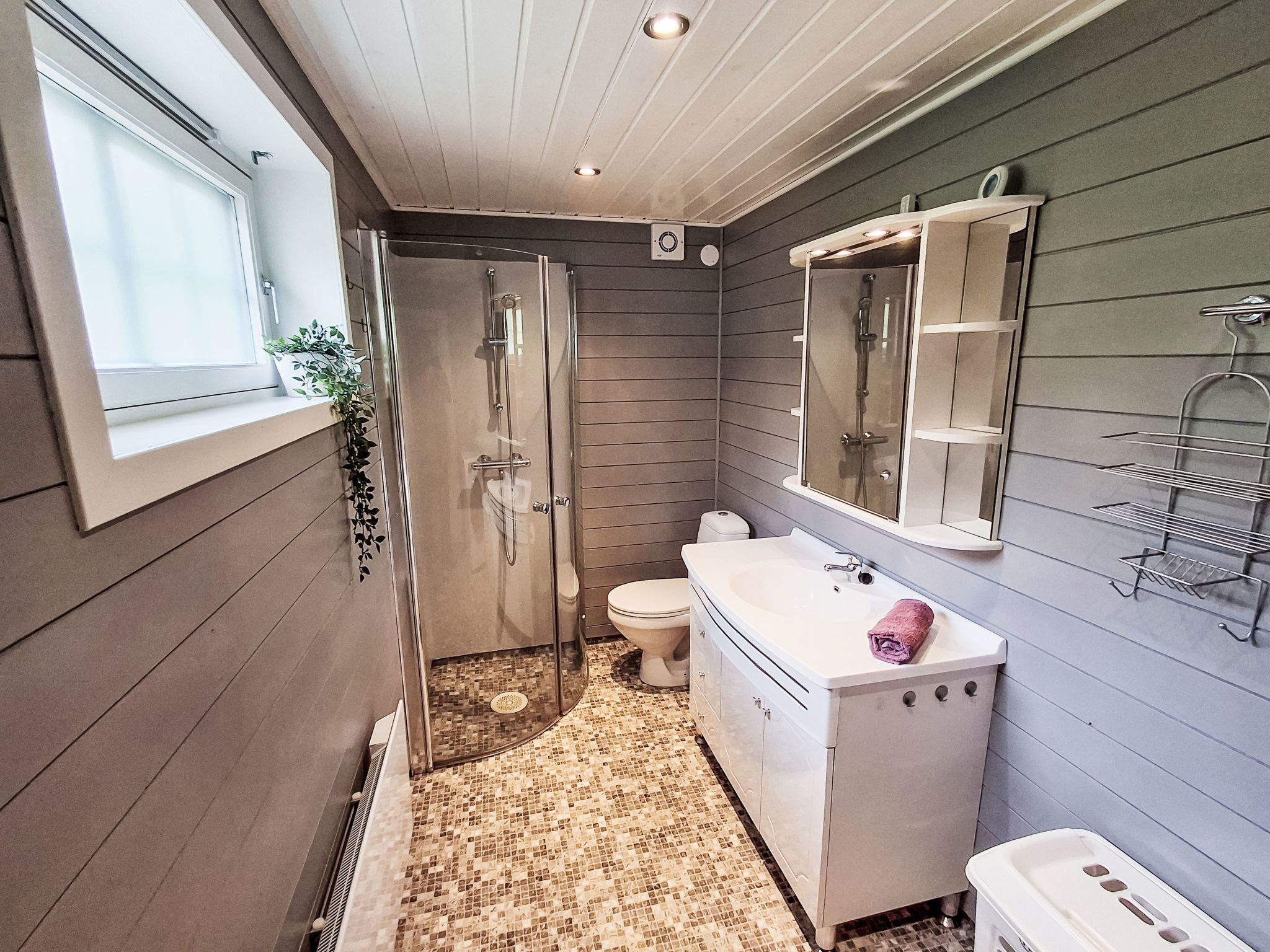 A bathroom with a walk-in shower, a toilet, a sink with a mirror, and a window.