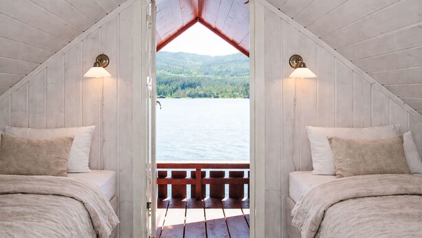 Een chalet met twee bedden, houten wanden en uitzicht op een meer en bos.