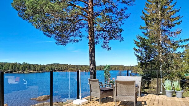 Une terrasse en bois, agrémentée de meubles en osier, donnant sur un lac.