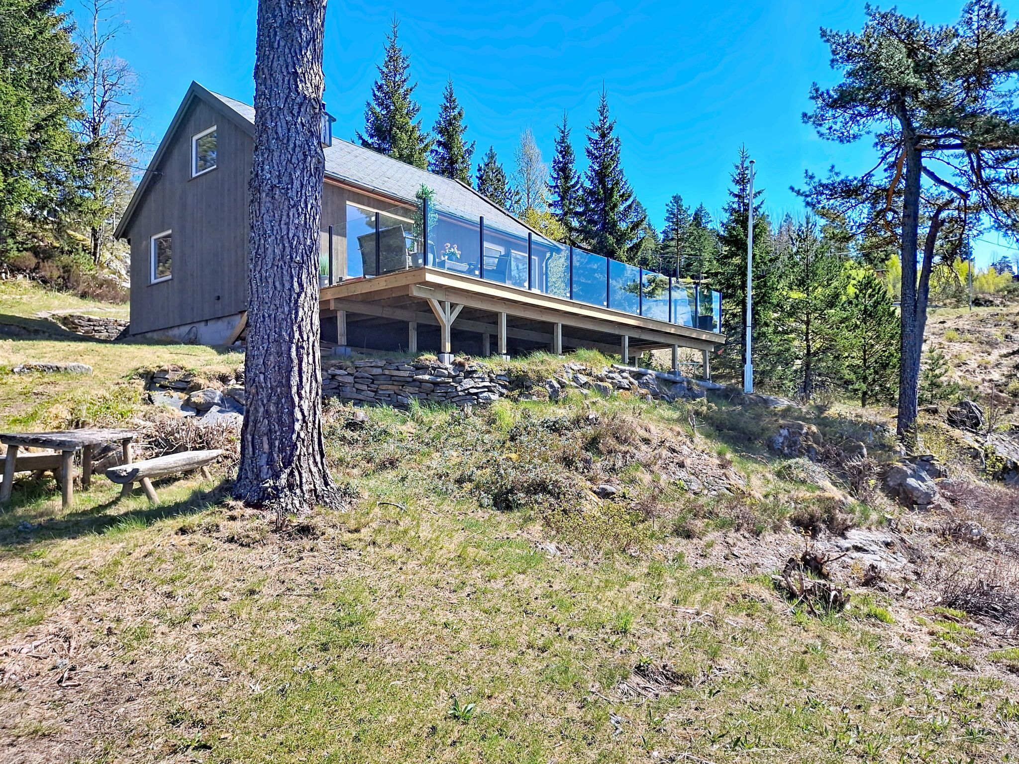 A modern cabin with a large glass facade, a wooden deck, and a stone foundation.