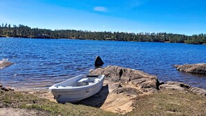 Un bateau sur une plage rocheuse, au bord d’un lac paisible, avec une rive boisée en arrière-plan.
