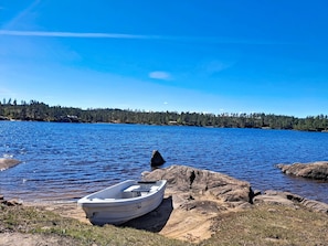 Ein Boot an einer felsigen Küste, an einem stillen See mit bewaldeter Uferlinie im Hintergrund.