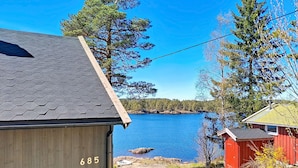 Une cabane en bois, avec le numéro « 685 » peint sur le côté, un ciel bleu clair et un lac bordé d’arbres en arrière-plan.
