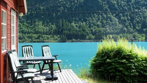 Eine Holzterrasse mit Tisch und Stühlen mit Blick auf einen See, umgeben von üppiger Vegetation und einem bewaldeten Hügel.