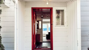 Un edificio blanco con una puerta roja y un ventanal pequeño.