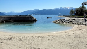 Una playa con agua cristalina, un promontorio rocoso y montañas al fondo.