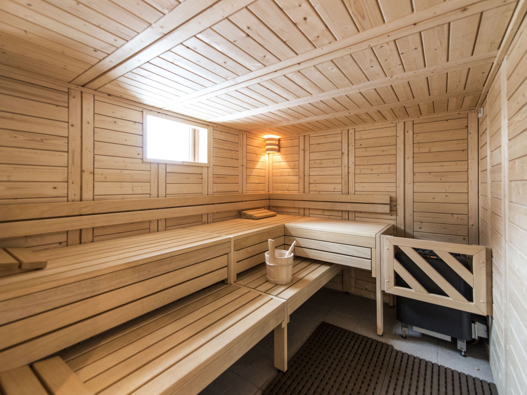 Una sauna con bancos de madera, un ventanal pequeño y una lámpara fijada a la pared.