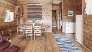 Un interior acogedor de cabaña con paredes de madera, un comedor con mesa y sillas, una cocina con fregadero y armarios, y una escalera que sube a otro nivel.