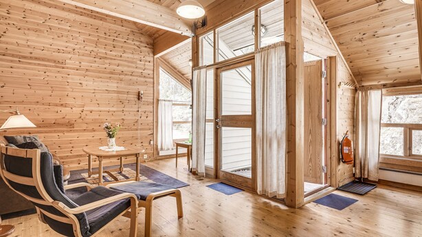 Un intérieur en bois avec un canapé, une petite table sur laquelle est posé un vase, et un banc.