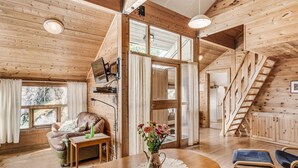 L’intérieur d’un chalet accueillant, avec un plancher en bois, une table à manger agrémentée d’un vase de fleurs, un canapé et un escalier.