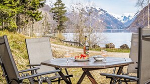 Un espace extérieur aménagé avec une table et des chaises, une bouteille de bière Ballantine et une vue panoramique sur les montagnes et un lac.
