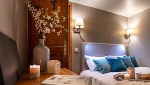 Un dormitorio con puerta de madera, mesita de noche con vela, lámpara y cama con almohadas azules.