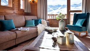 Una habitación acogedora con detalles de madera, un sofá, una silla y vistas a montañas nevadas a través de amplios ventanales.