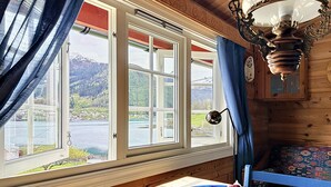 A room with a large window, a wooden ceiling, a table with a bowl of fruit, and a patterned chair. - Naustvollen by Interhome (Balestrand)