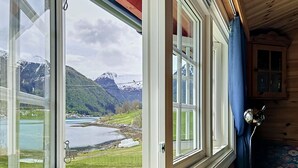 A cabin with a large window offering a view of a lake and mountains. - Naustvollen by Interhome (Balestrand)