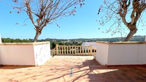 Une terrasse sur le toit, dotée d’un sol carrelé, d’une rambarde et offrant une vue sur un paysage verdoyant.
