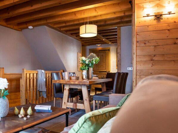 A cozy living room with a wooden ceiling, a dining table with chairs, and a sofa.