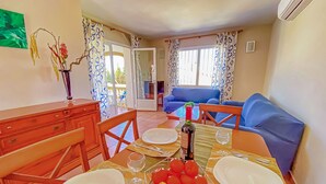 Un coin repas avec une table dressée pour quatre personnes, un canapé bleu et une table à manger agrémentée d’un vase de fleurs.