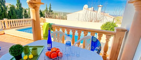 A table set with a green tray, a potted plant, lemons, oranges, and a bottle of water on a balcony overlooking a pool and a clear sky.