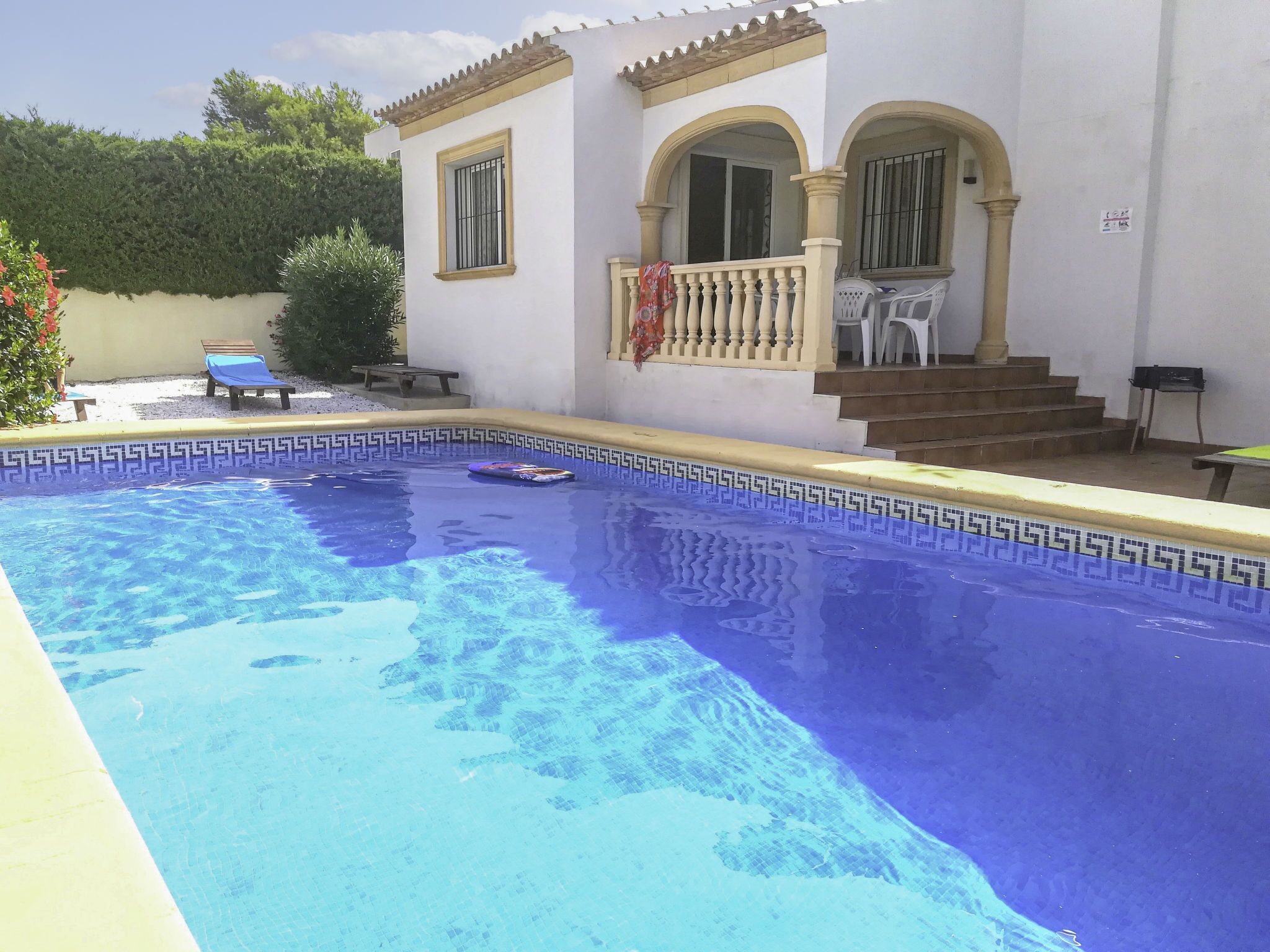 A swimming pool with a tiled edge, a covered patio with a railing, and a staircase leading to a door.