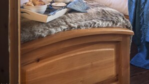 Una habitación acogedora con dos camas de madera, una ventana con cortinas y una mesita de noche con lámpara, y vistas a montañas nevadas.