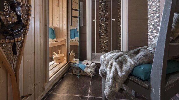 Una sala de sauna con bancos de madera, una puerta de cristal que da a una zona de ducha y un banco cubierto de pieles.