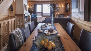 A cozy wooden cabin interior with a dining table set for a meal, a fireplace, and a view of the outdoors.