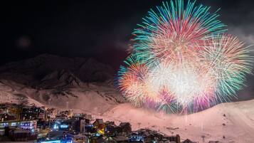 Une ville de montagne enneigée, avec des bâtiments illuminés et un grand feu d’artifice.