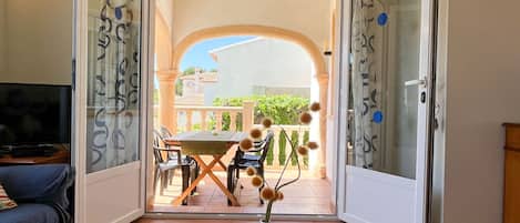 An open door leading to a balcony with a table, chairs, and a vase with dried flowers.