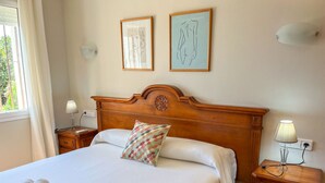 A neatly made bed with a patterned pillow, a wooden nightstand with a lamp, and two framed artworks on the wall. - Lavanda by Interhome (Jávea)