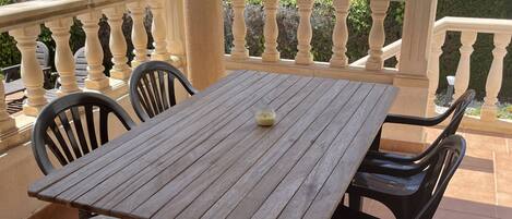 A wooden table with two chairs on a tiled patio with a balustrade.