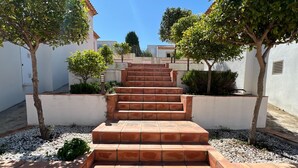 A set of terracotta-tiled outdoor stairs leading up to a white building, surrounded by trees and gravel.