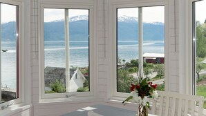 Ett rum med utsikt över en sjö och berg, ett vitt bord med en blå duk och en vas med blommor.