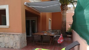 Um pátio com mesa e cadeiras, área coberta e muro de pedra.