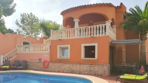 Piscina com muro de pedra e varanda com grades brancas.