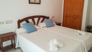 Cama bem arrumada com lençóis brancos, dois travesseiros e um par de toalhas dobradas sobre a cama.