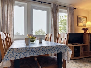 A dining area with a table set for two, chairs, a television, and a window with curtains. - Lihesten by Interhome (Sørbøvåg)