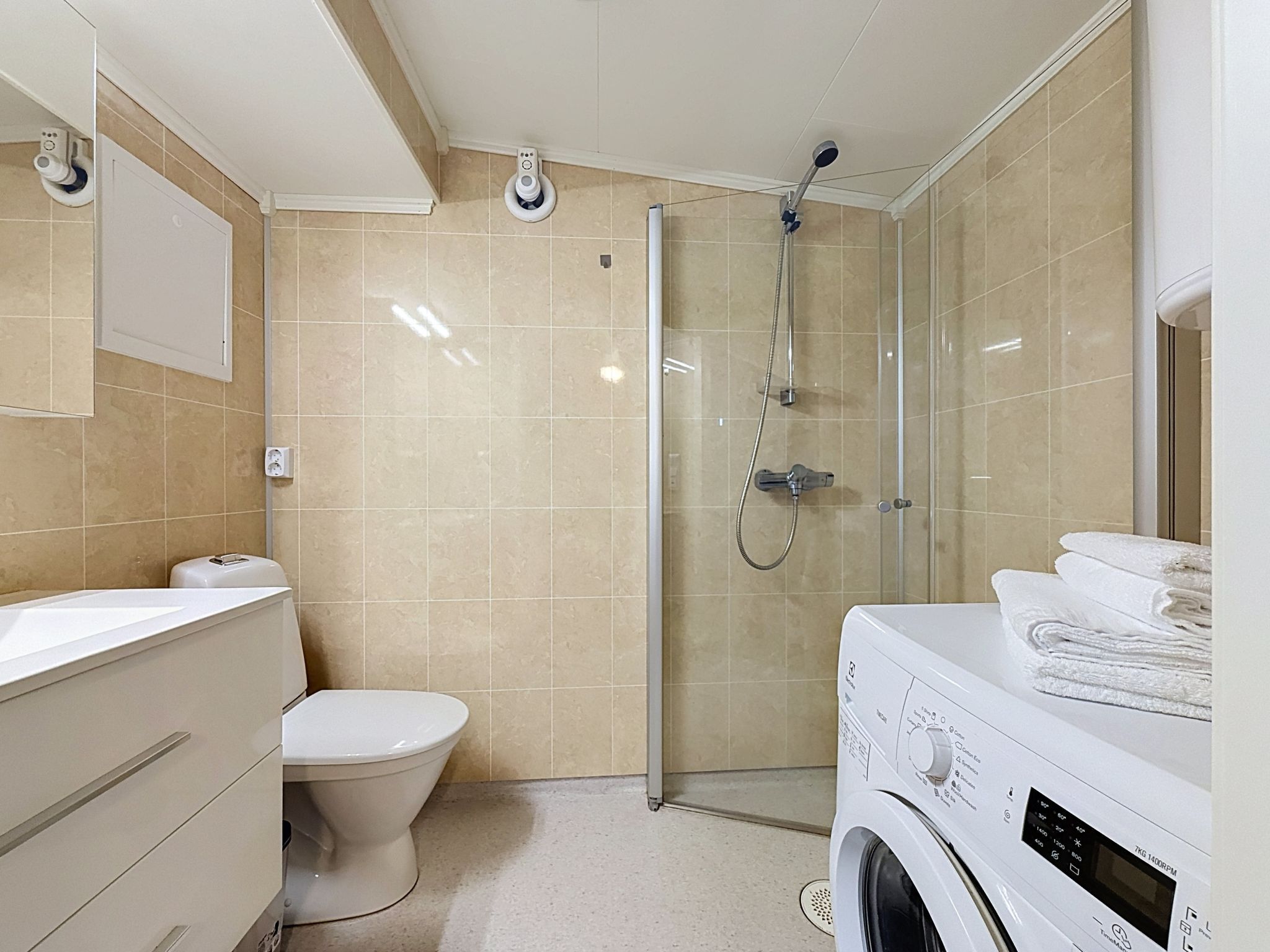 A modern bathroom with a glass shower enclosure, a toilet, a sink, and a washing machine.